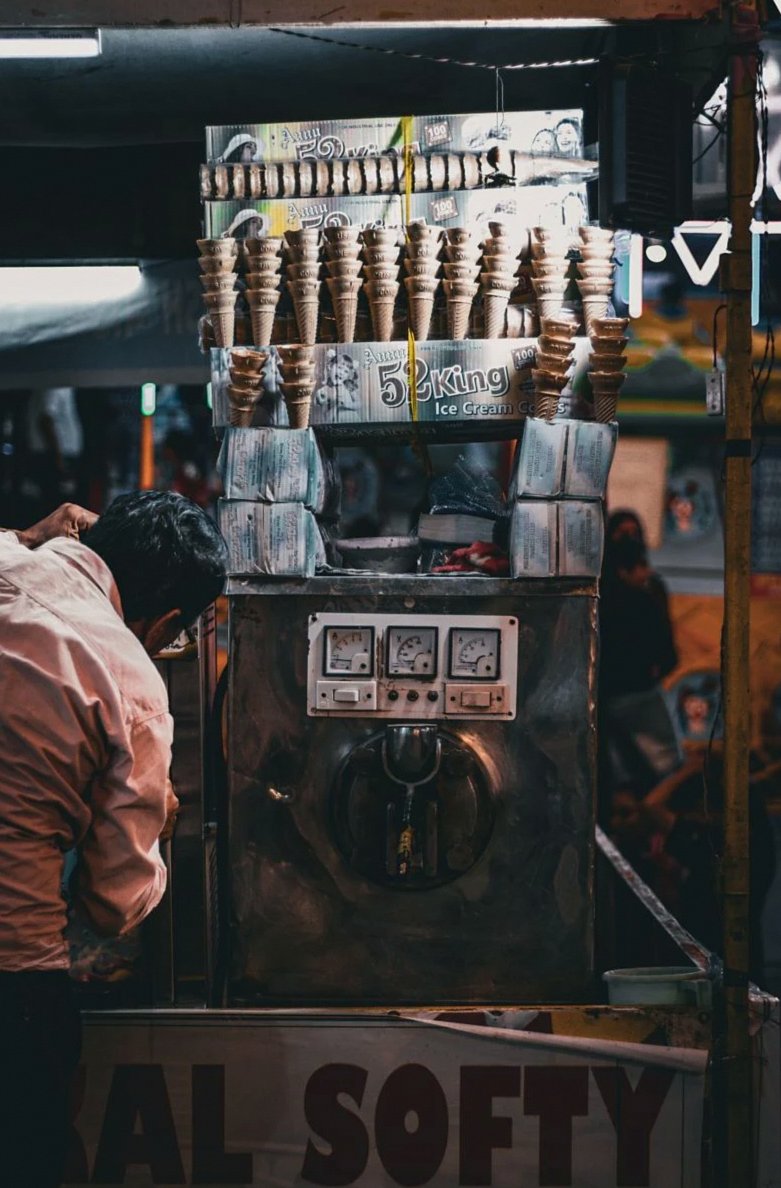 Un vendedor ambulante prepara conos de helado en una máquina vintage durante la noche.