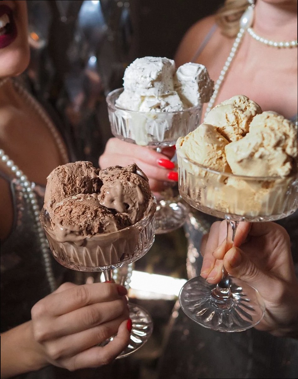 Tres mujeres brindan con copas decorativas llenas de helado, adornadas con perlas.